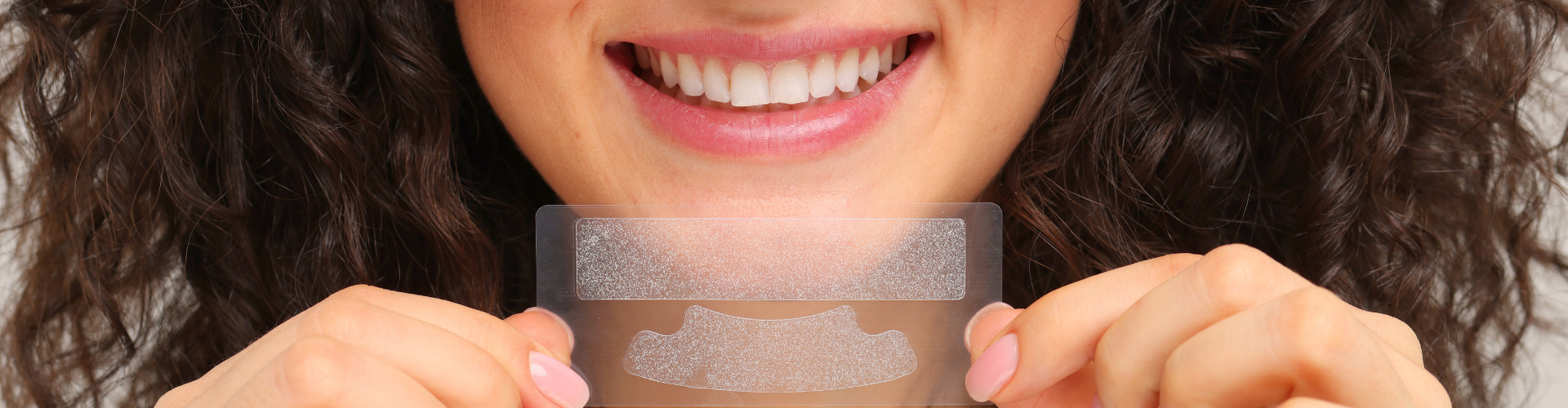 Woman holding teeth whitening strips in front of her smile.